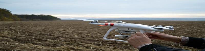 manos sujetando un dron listo para volar sobre un campo sin sembrar